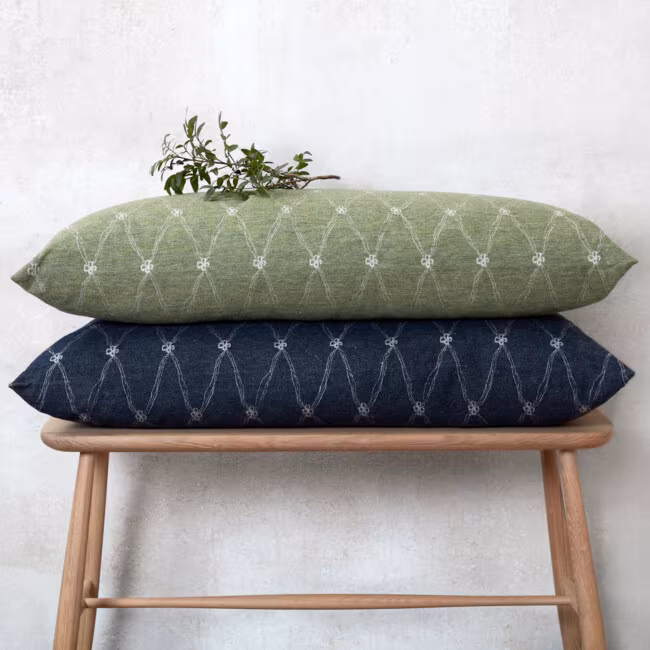 Oblong decorative pillows lying on top of each other, on a pallet. The colors dark blue and green with a clover pattern