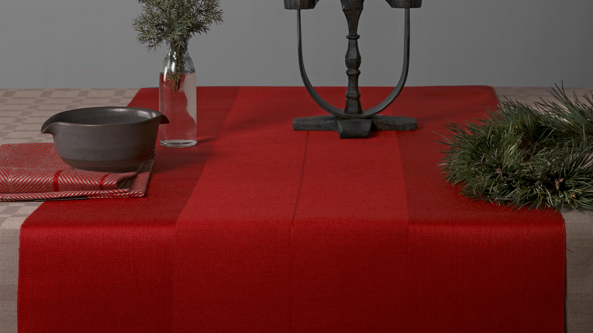 Dylta bordslöpare röd med en smide ljusstake med två ljus. På bordet finns även granris